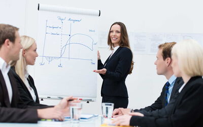 Eine Managerin hält einen Vortrag, eine Präsentation, vor anderen Managern. Sie wirkt souverän, selbstsicher und voller Selbstvertrauen