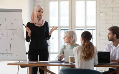 Eine Frau steht Business-Kontext vor einer Gruppe und hält eine Präsentation.