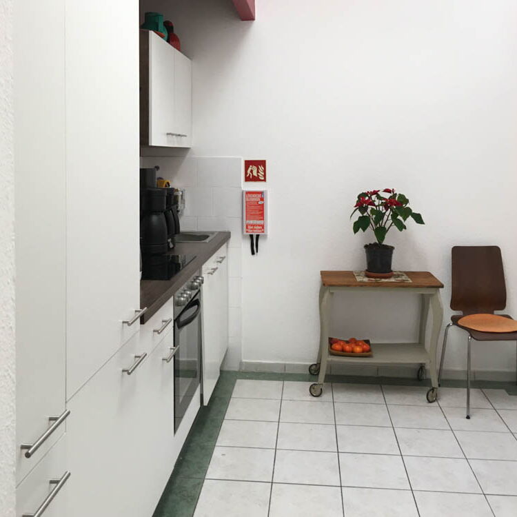 Die vollständig eingerichtete Küche in der Coachingpraxis. mit Espresso-Maschine, Herd, Spülmaschine. Die Wände sind rot gestrichen.